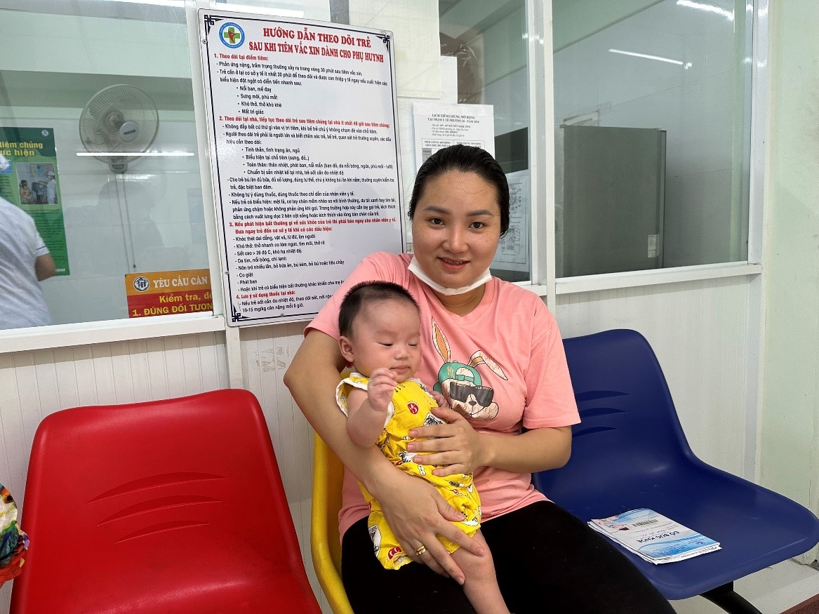 Một phụ huynh vui mừng đưa trẻ đi tiêm vắc xin 5 trong 1 tại quận Bình Thạnh